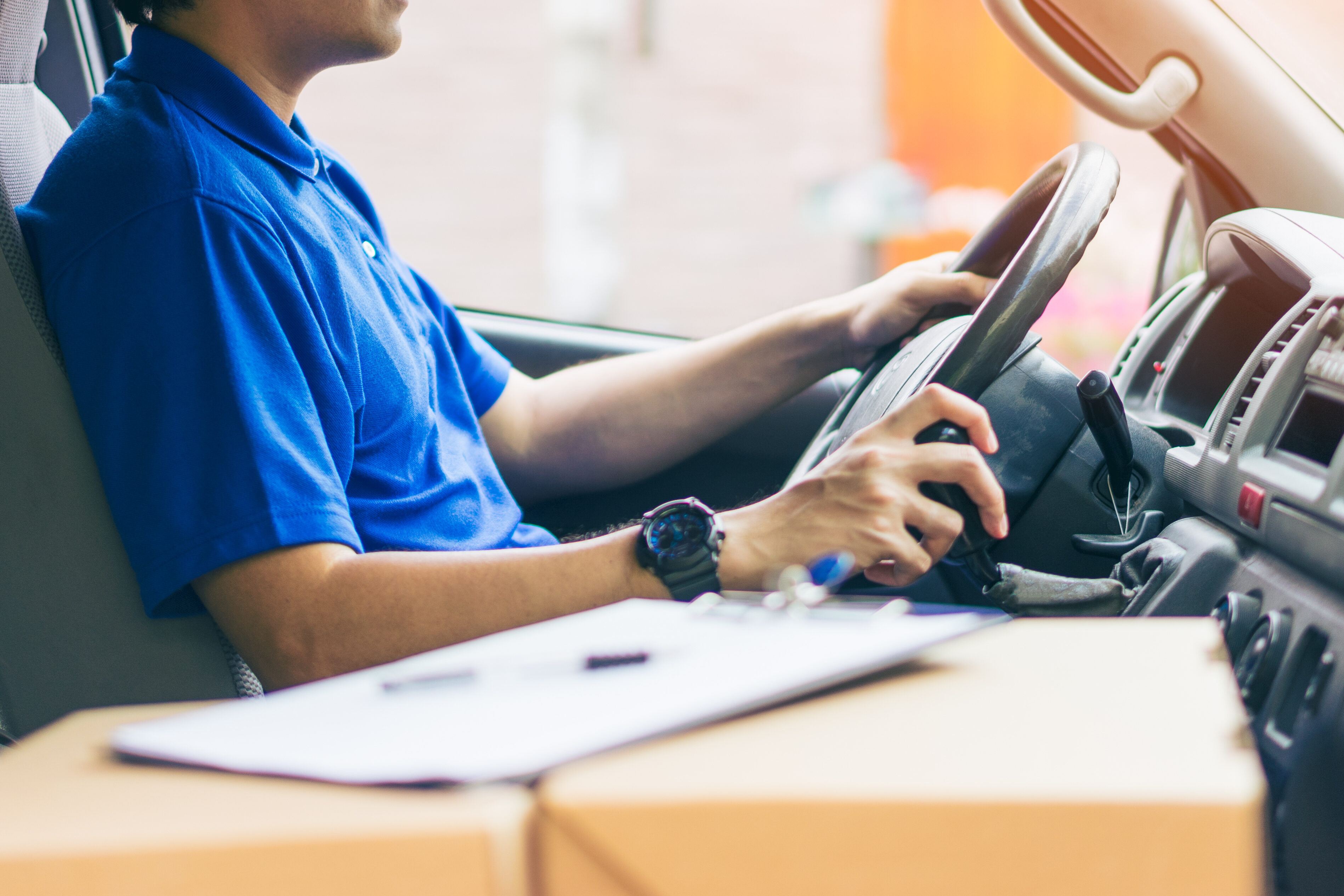Young handsome delivery man driving his van with packages on the front seat